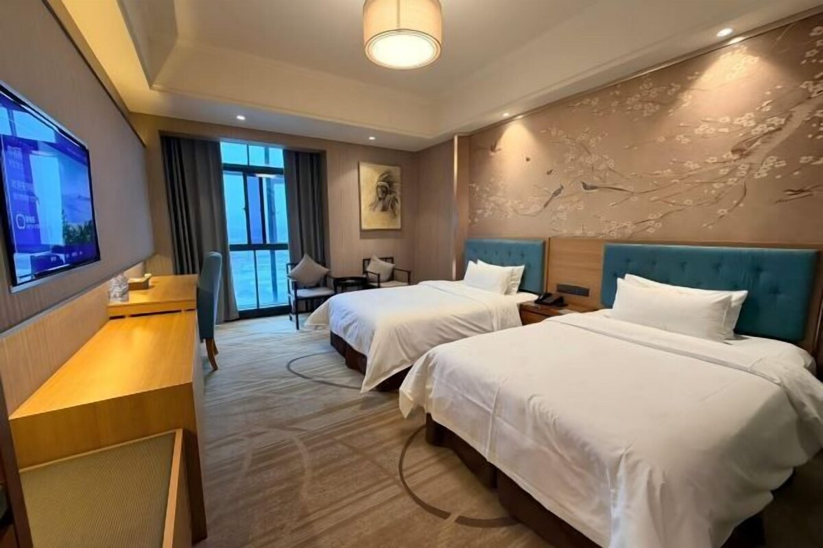 Habitación de hotel con dos camas, un escritorio, un televisor y un ventanal con vistas.