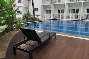 A poolside area with a lounge chair, a pool, and a building with balconies in the background. - Shore Residences Mall of Asia Stays by Pbyy (Pasay)