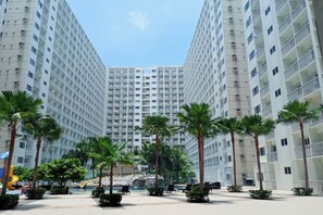 Un edificio residencial de gran altura con un patio central que cuenta con palmeras, un parque infantil y una fuente.