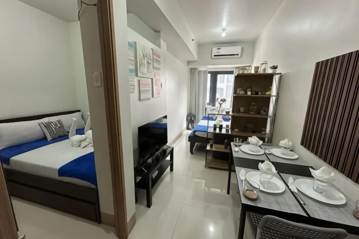 A hotel room with a bed, a TV, a dining table set for two, and a bookshelf.