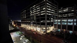 Un aparcamiento de varios pisos con ventanas iluminadas, junto a una calle con coches aparcados y un autobús.
