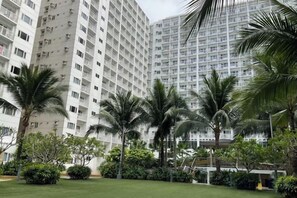 A multi-story hotel with a uniform facade, surrounded by well-maintained greenery and palm trees. - Shore Residences Mall of Asia Stays by Pbyy (Pasay)