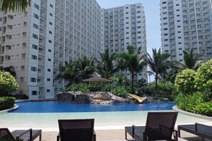 Una piscina con sillas de descanso, rodeada de palmeras y una formación rocosa.