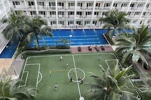 Une piscine intérieure avec un terrain de football, entourée de palmiers et bordée d’un immeuble à plusieurs étages doté de balcons.