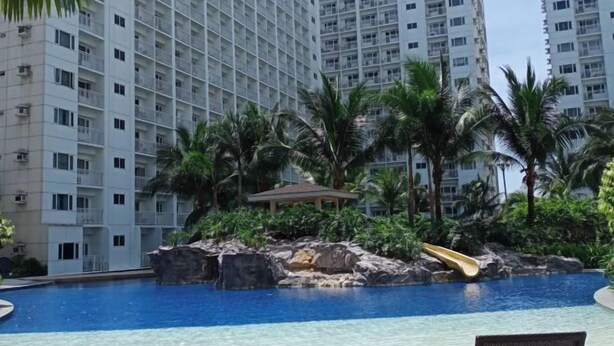 Una piscina con tobogán, rodeada de palmeras y una formación rocosa.