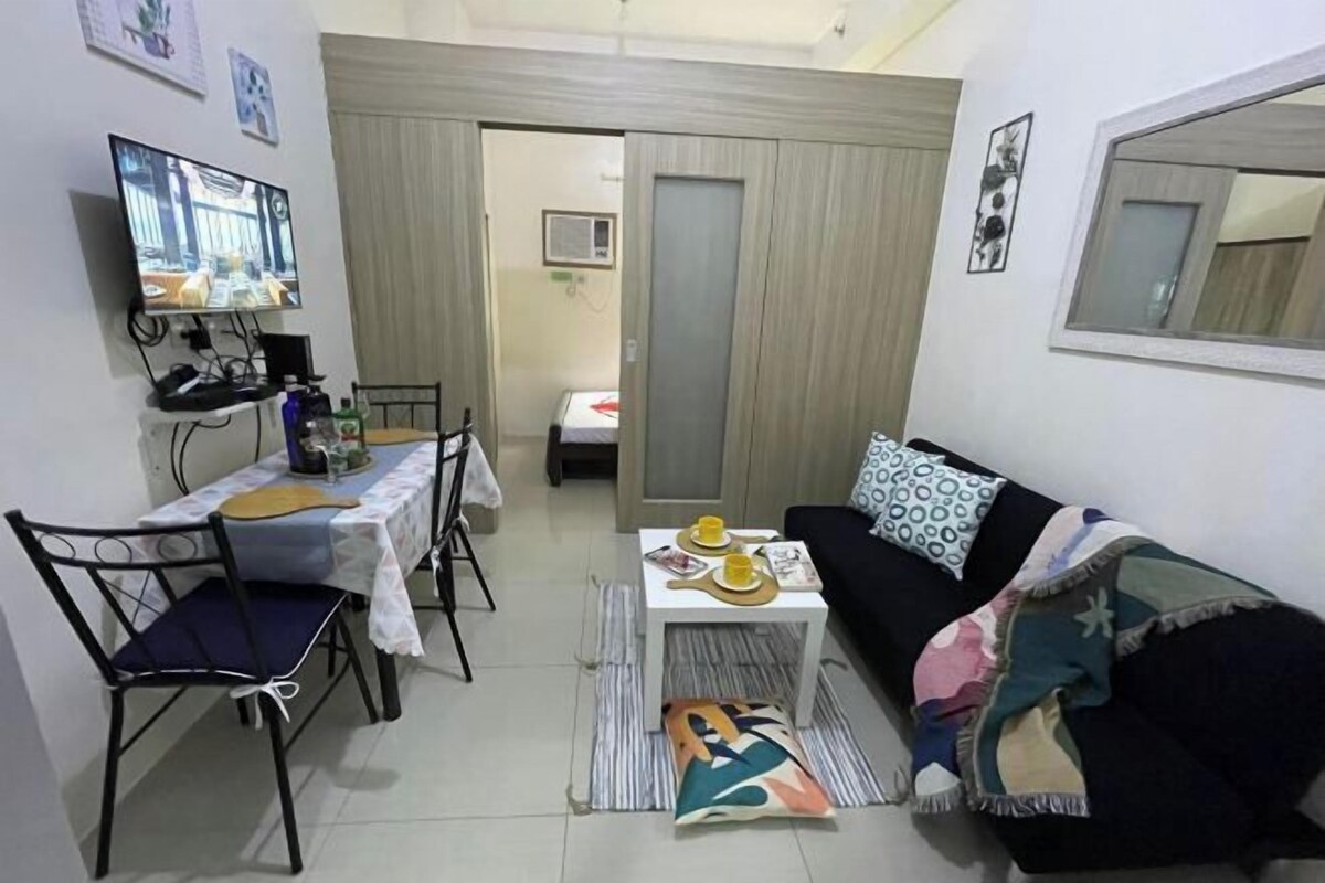 A compact living space with a dining table, chairs, a sofa, a TV, and a small kitchenette.