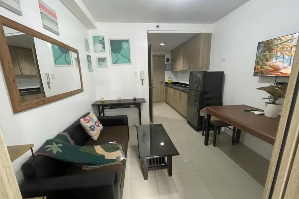 Un espacio habitable compacto con sofá, una mesita, zona de cocina con armarios y una mesa de comedor.