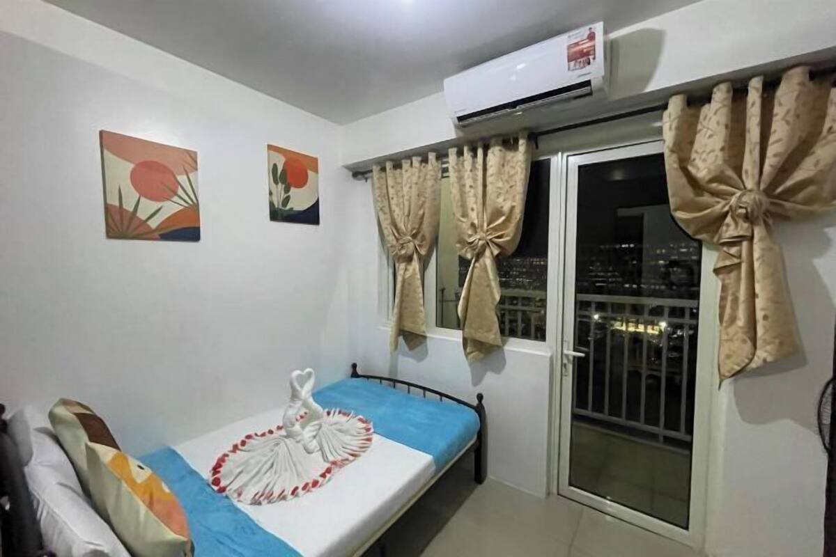 Ein Zimmer mit einem Bett, einem Vorhangfenster, einer Klimaanlage und zwei Bildern an der Wand.