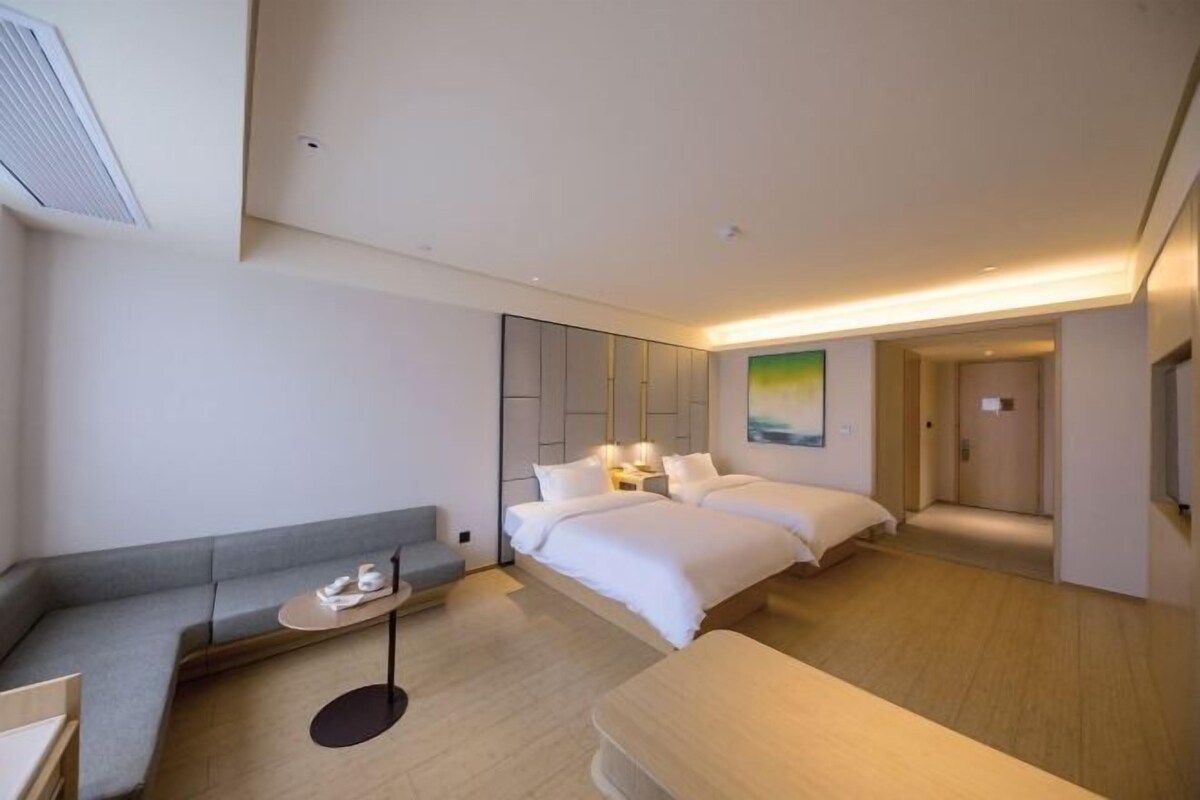 A modern hotel room with a sofa, a small table, two beds, and a painting on the wall.