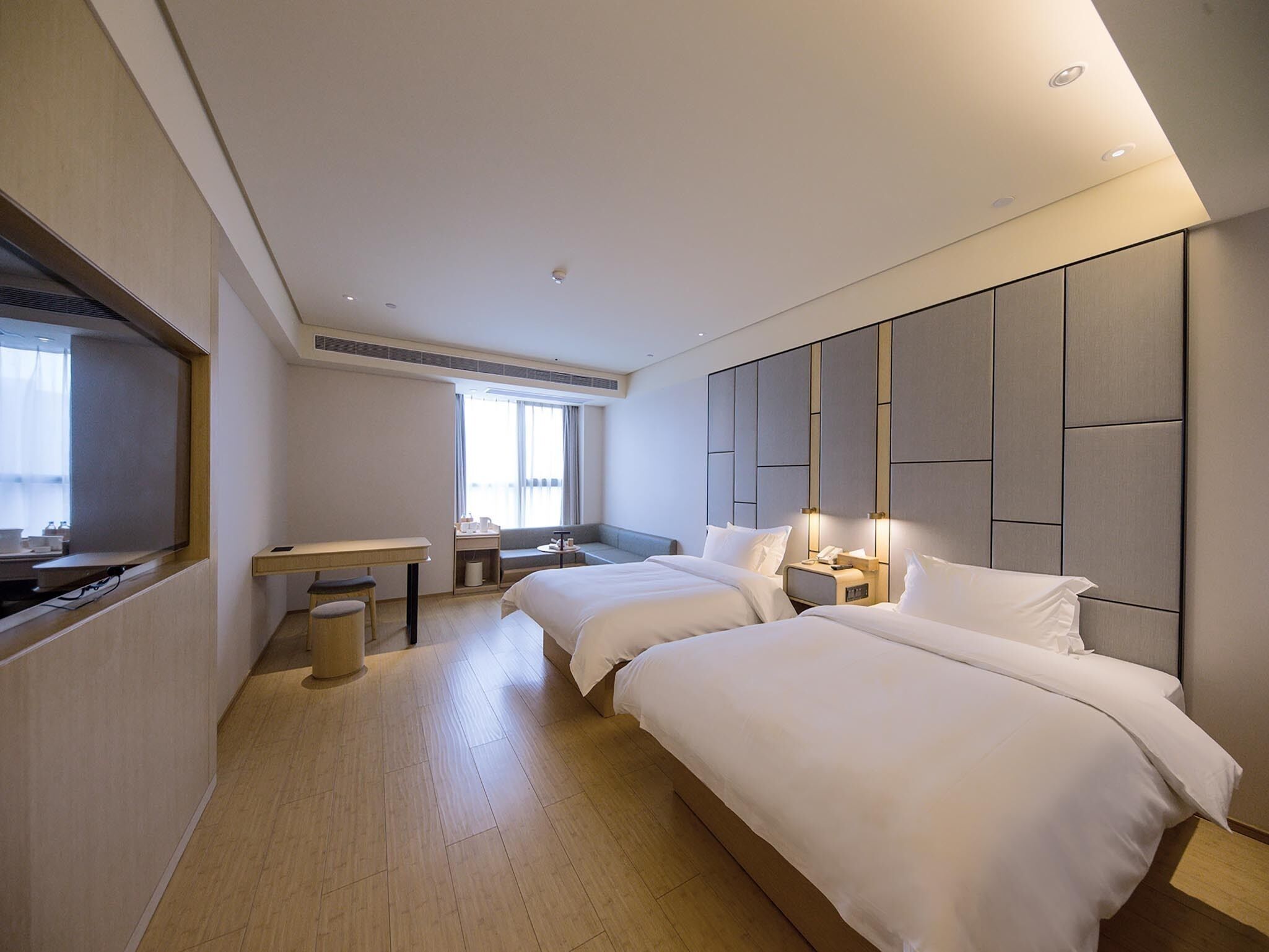 A hotel room with two beds, a desk, a chair, a small table, and a window.