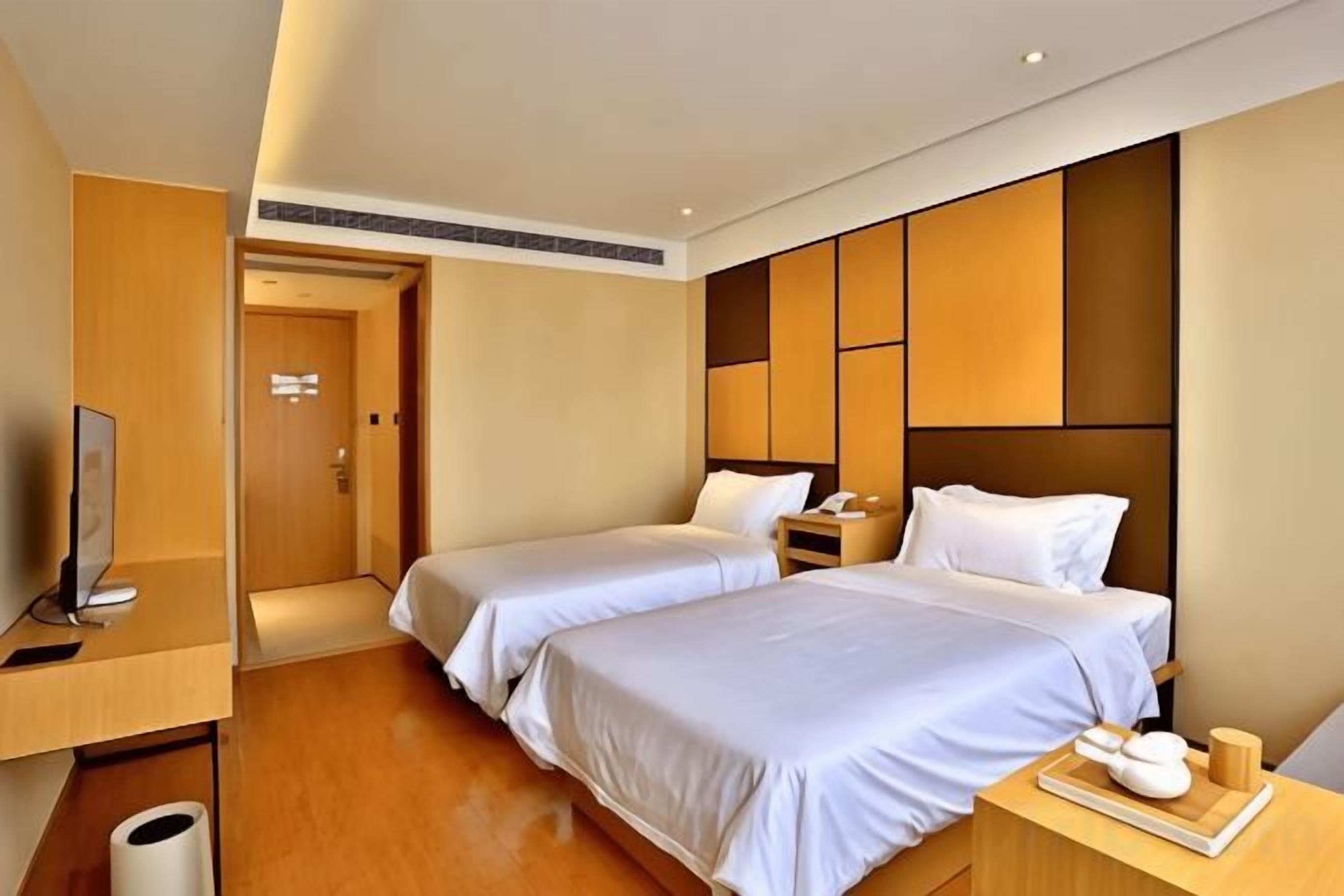 A hotel room with two beds, a desk, and a television.