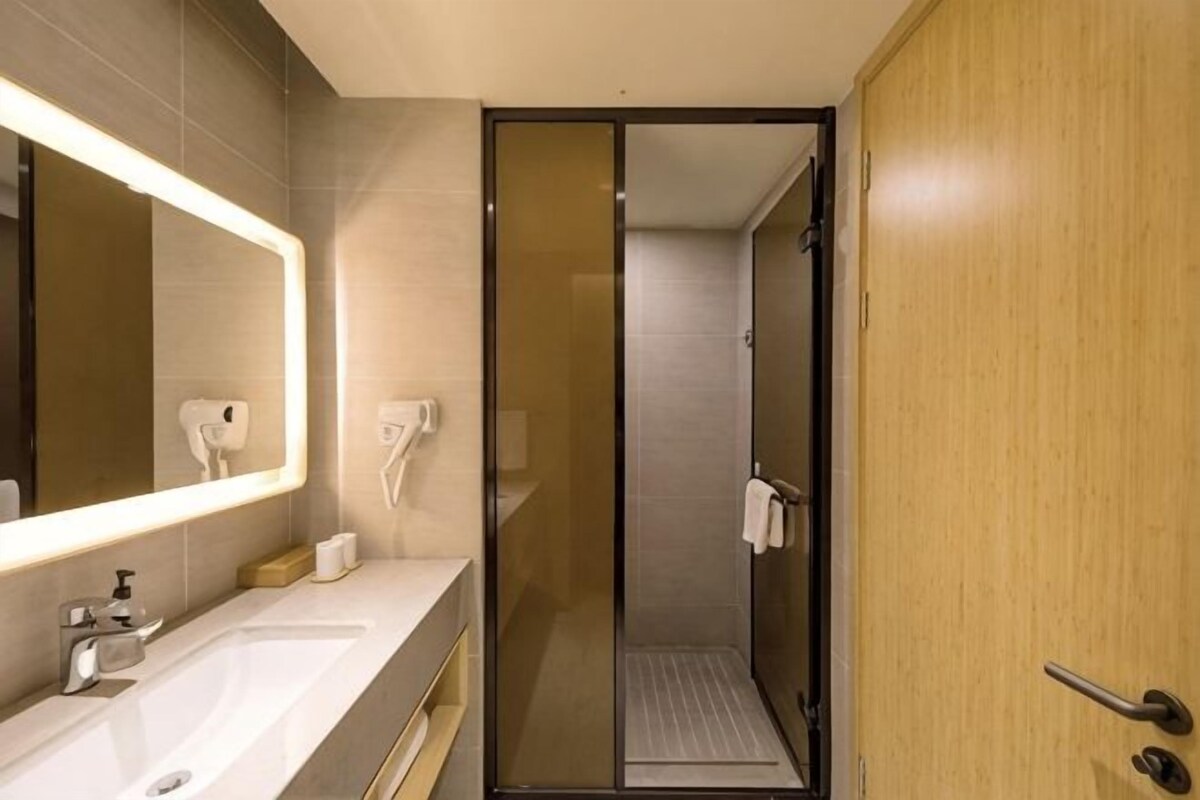 A modern bathroom with a large mirror, a sink, a shower, and a wooden door.