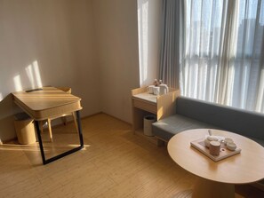 A room with a wooden table, a sofa, a small desk with a chair, and a window with curtains. - Ji Hotel (Jiaxing)