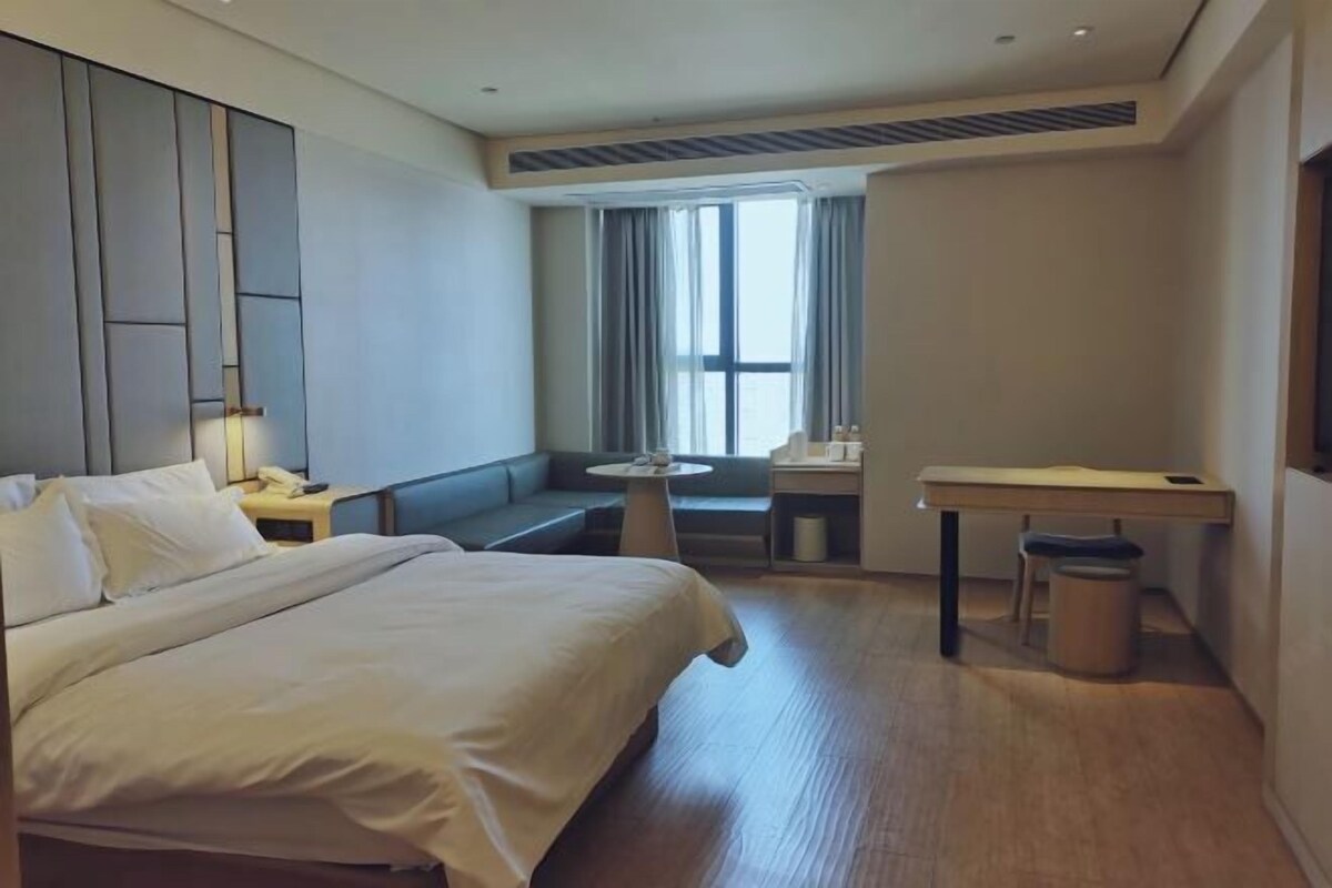 A hotel room with a bed, a desk, a chair, a small table, and a window with curtains.