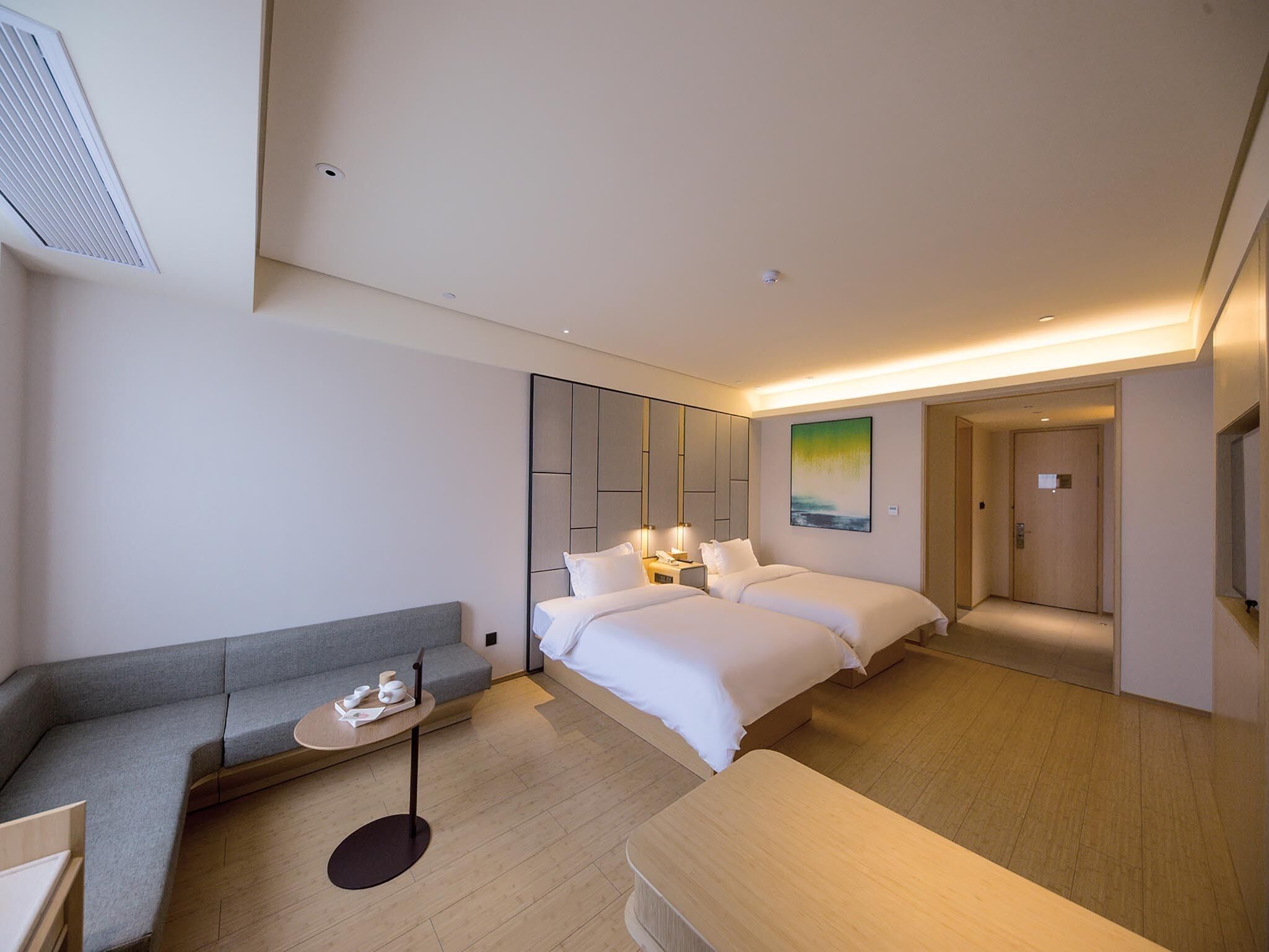 Una habitación de hotel moderna con un sofá, dos camas, una mesita y un cuadro en la pared.