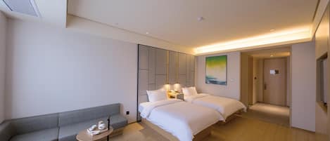 A modern hotel room with a sofa, two beds, a small table, and a painting on the wall.
