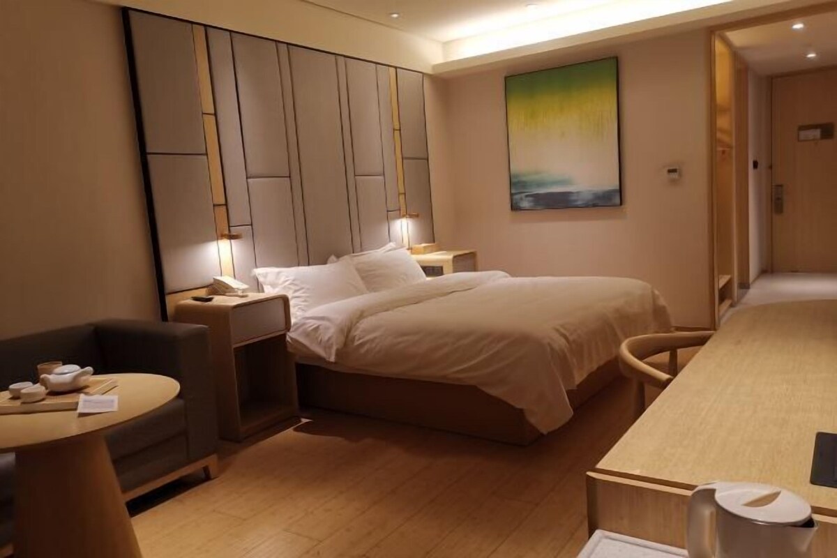 A hotel room with a bed, bedside table, chair, and a desk with a lamp.