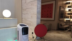 A robot vacuum cleaner in a modern hotel lobby with a marble floor, a red circular object, and a wall-mounted light. - Ji Hotel (Jiaxing)