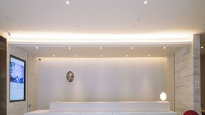 A reception area with a modern design, featuring a white reception desk, a logo on the wall, and a red chair. - Ji Hotel (Jiaxing)