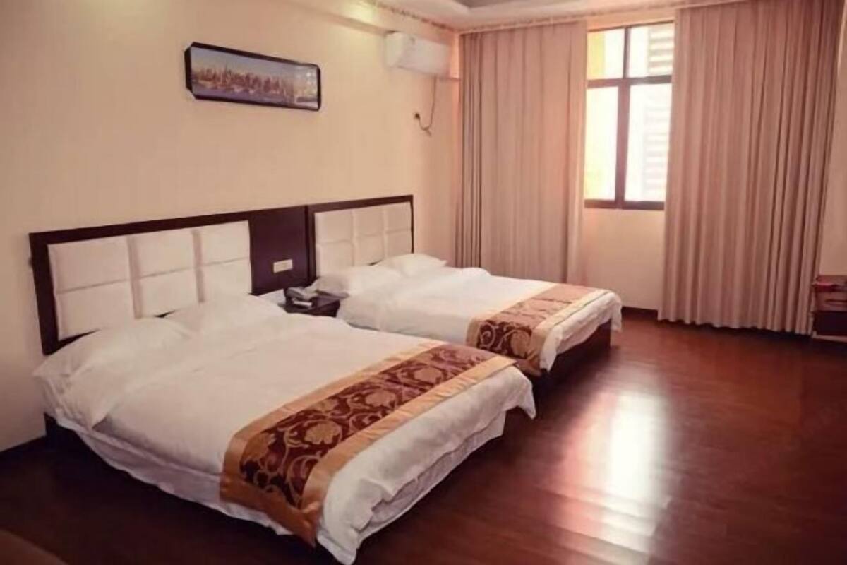 Habitación de hotel con dos camas, una mesita de noche, aire acondicionado de pared y una ventana con cortinas.