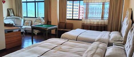 A hotel room with two beds, a desk, a chair, a pool table, and large windows with curtains.