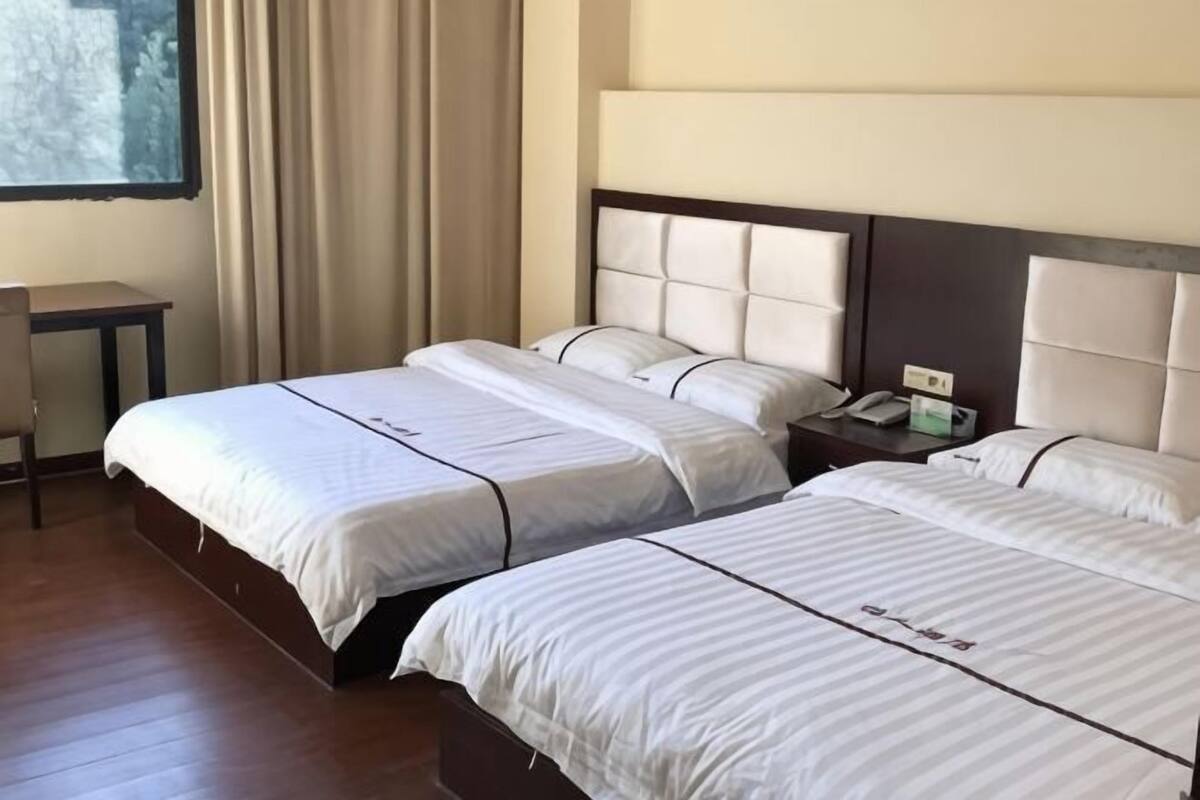Habitación de hotel con dos camas, una mesita de noche y un ventanal con cortinas.