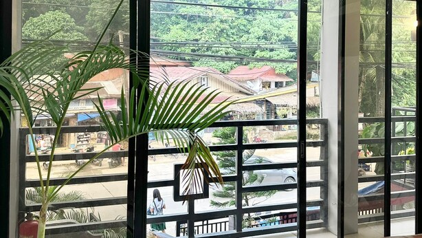 A room with a large glass door leading to a balcony with a view of a residential area and greenery.