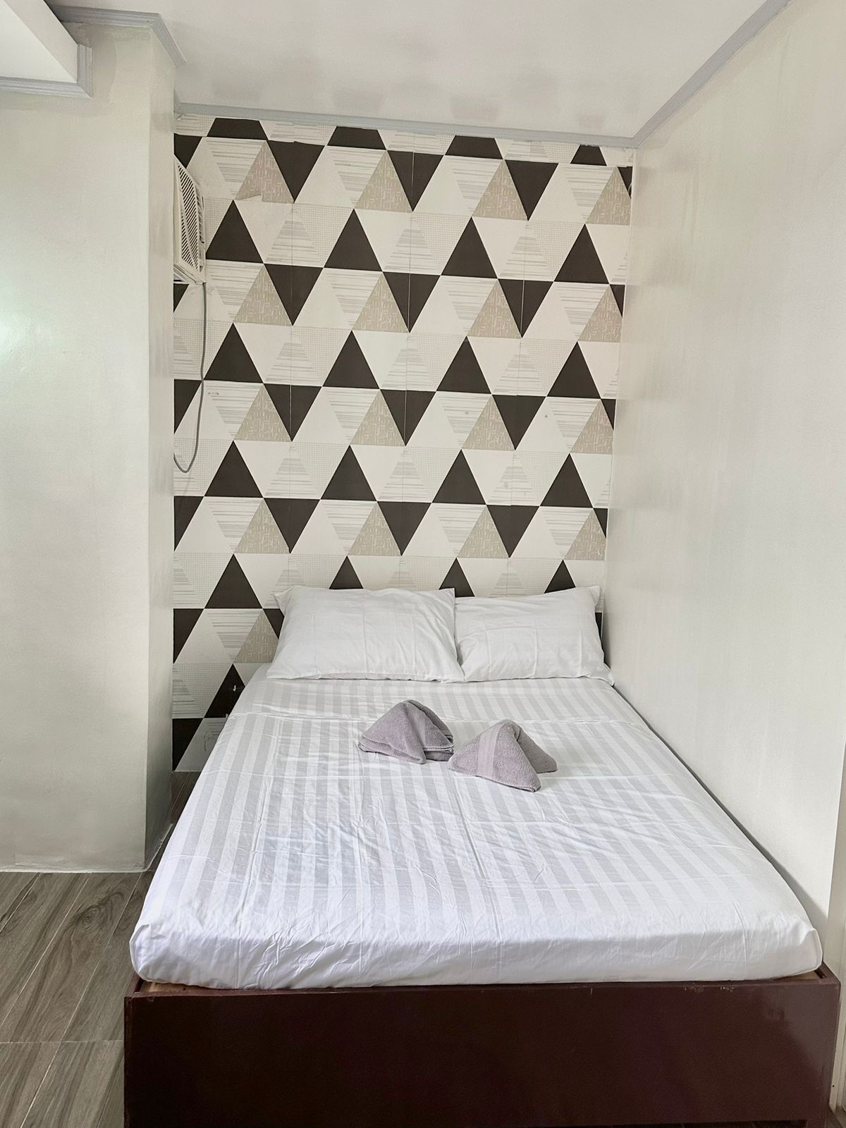 Una cama individual con cabecera de estampado geométrico, ropa de cama blanca y suelo de madera.