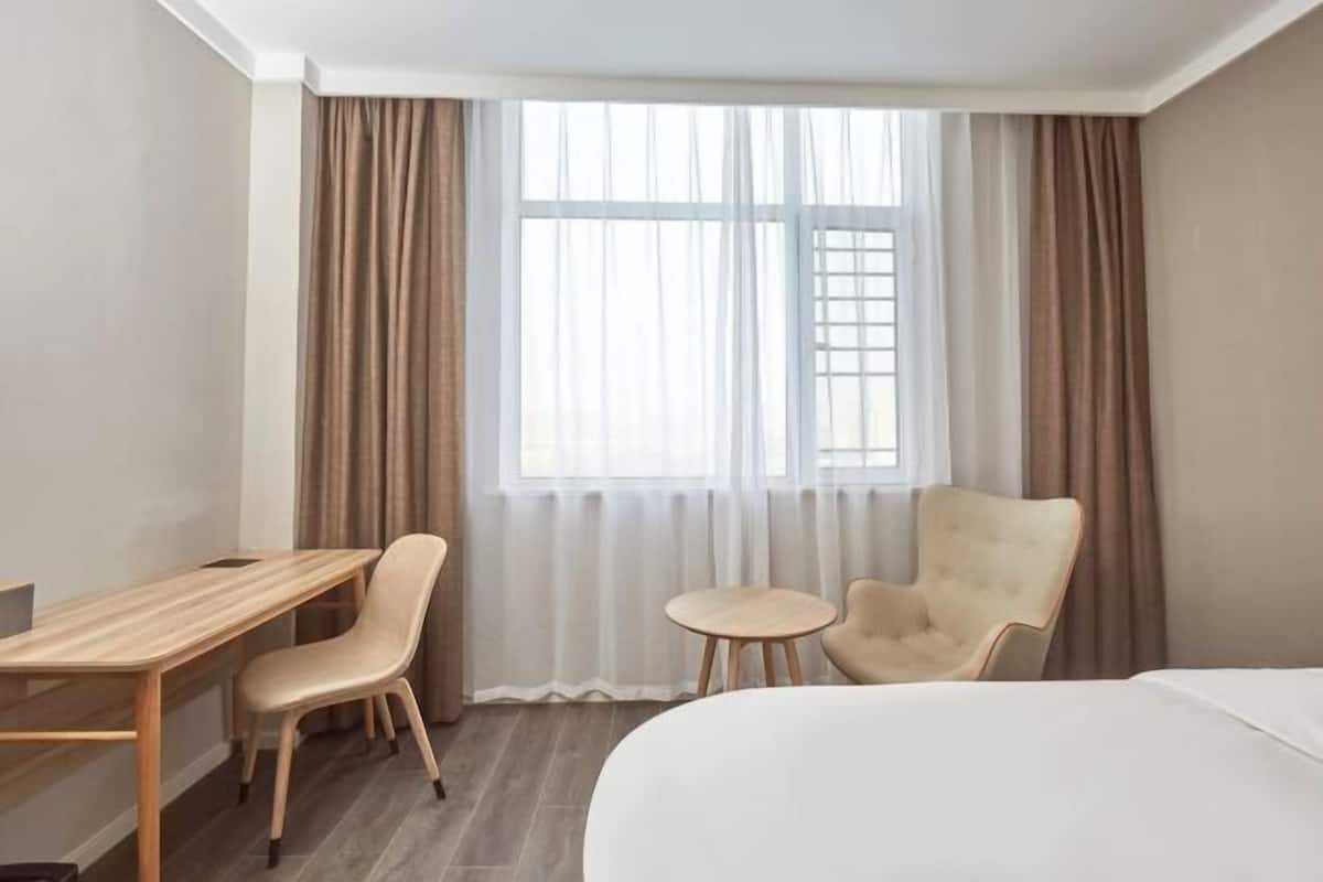 Et hotelværelse med seng, skrivebord, to stole og et vindue med gardiner.