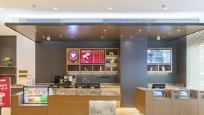 Un hall d’hôtel moderne comprenant un comptoir d’accueil, une machine à café et un présentoir réfrigéré.