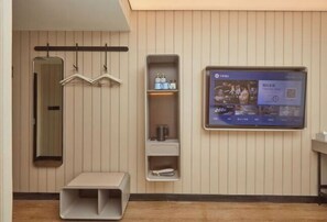 Une salle de bain moderne avec un meuble-lavabo, un miroir, une étagère contenant des articles de toilette et un téléviseur fixé au mur diffusant une émission.