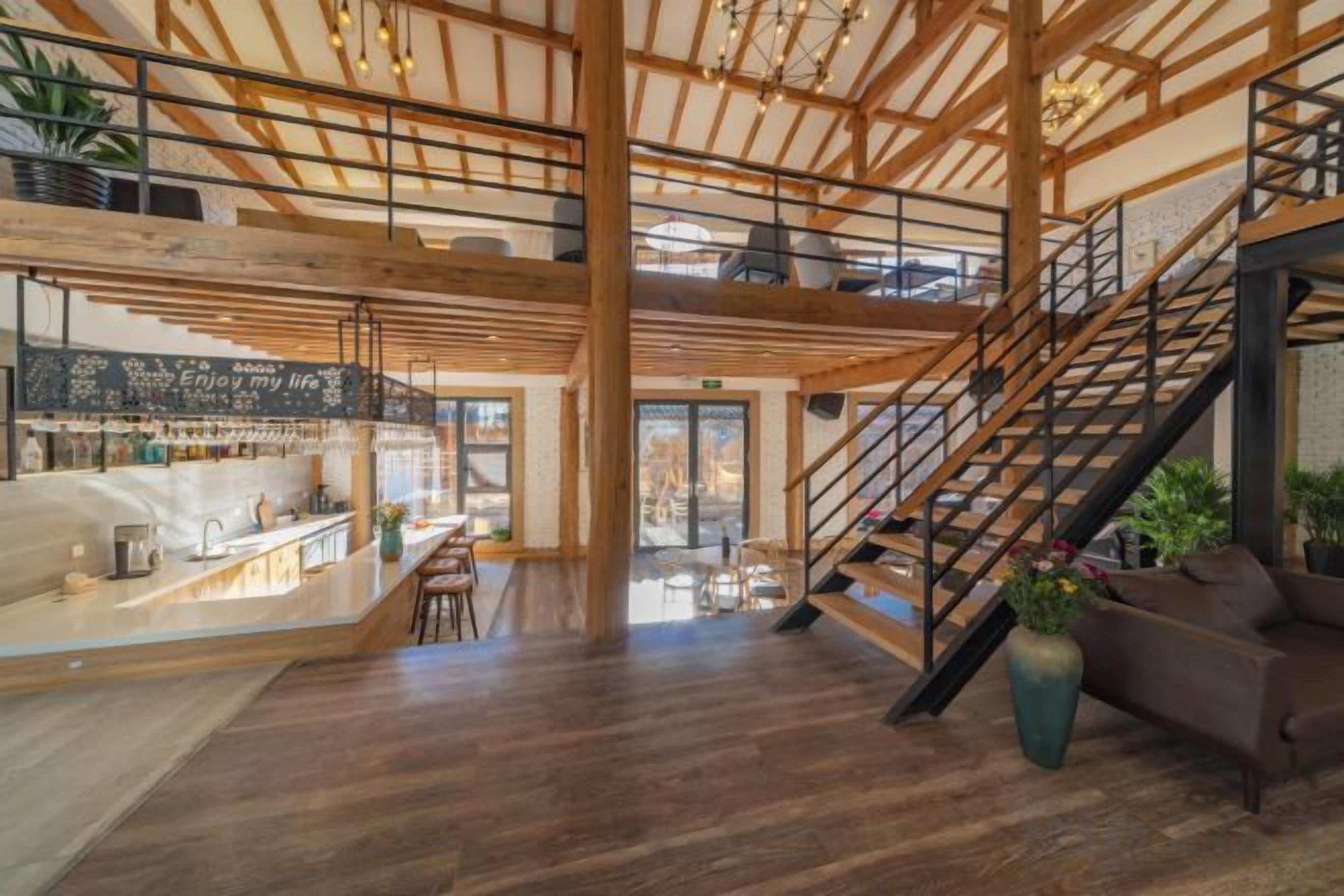 Un intérieur spacieux avec un plafond haut, des poutres en bois, un escalier et un coin salon.