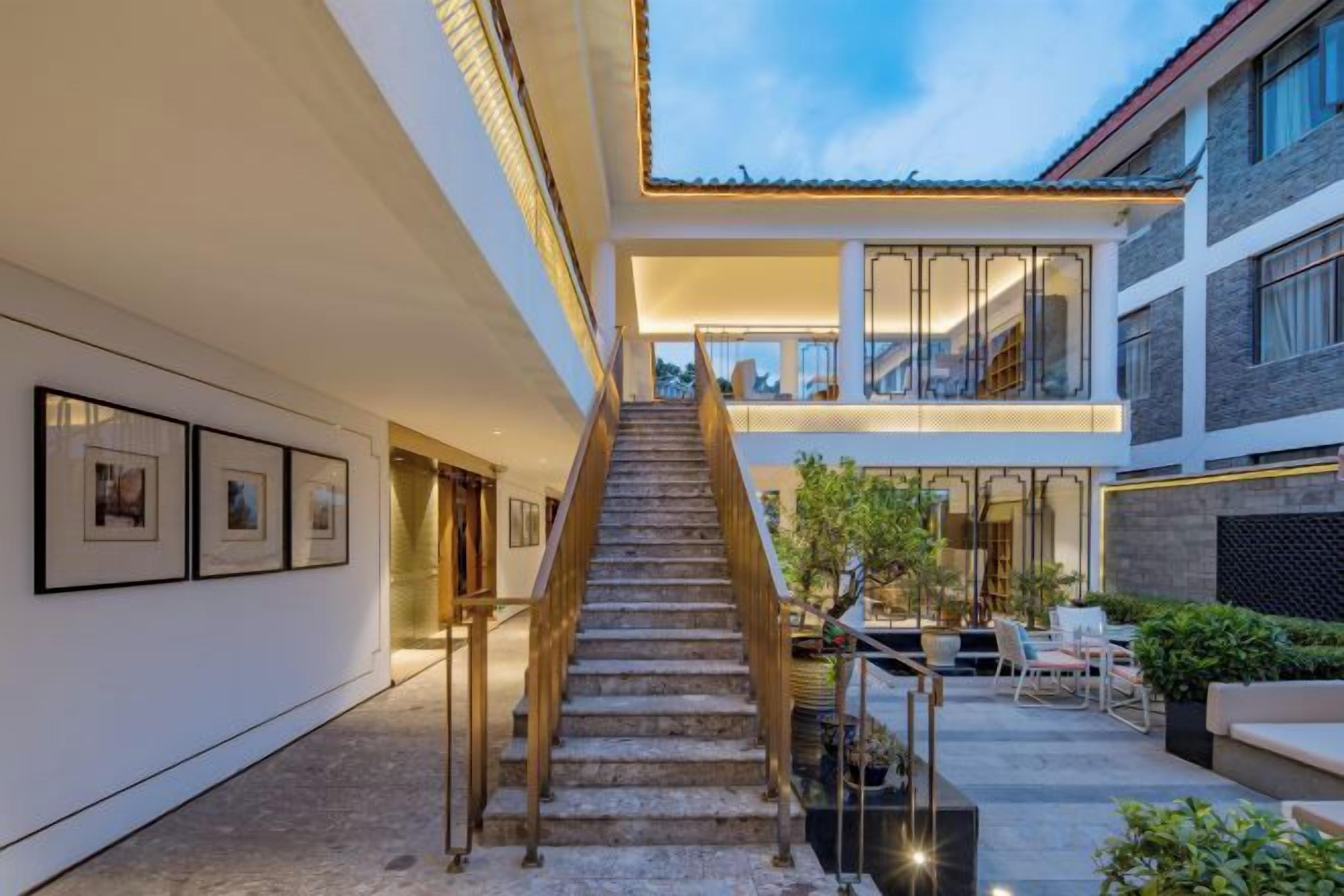 A modern interior with a staircase leading to a second floor, framed artwork on the walls, and outdoor seating area.