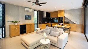 A modern living room with a sofa, a dining table, and a kitchen area with wooden cabinets and a microwave. - Spacious Pavilion P07 in Natural Park (Kamala)