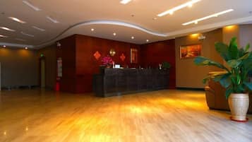 A hotel reception area with a curved reception desk, a large potted plant, and a wall-mounted painting.