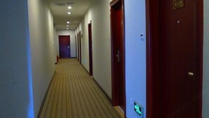 Een hotelgang met tapijtvloeren, houten deuren en een groen vluchtbord.