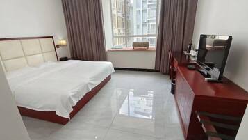 A hotel room with a bed, a desk, a television, and a window with curtains.
