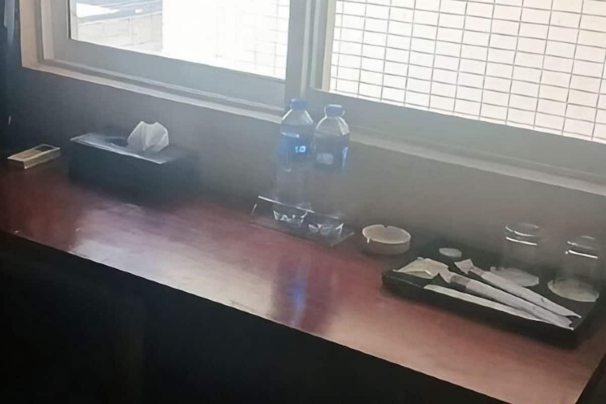 A wooden counter with a tissue box, two water bottles, a tray with napkins, and a window with blinds.