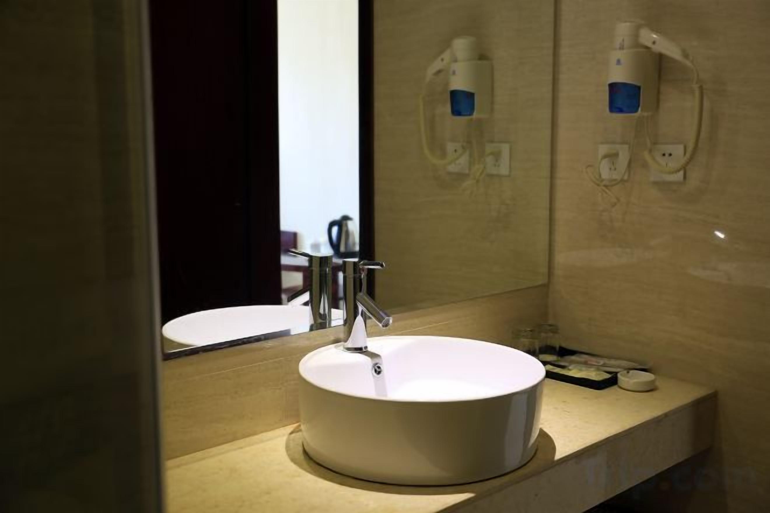 A bathroom with a round white sink, a mirror, and two wall-mounted soap dispensers.