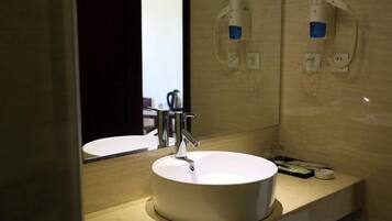 A bathroom with a round white sink, a mirror, and two wall-mounted soap dispensers.