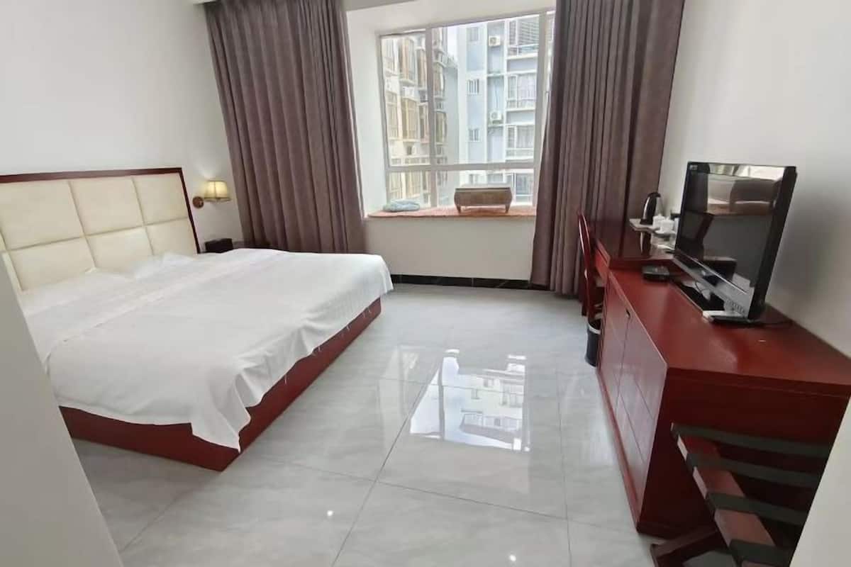 Une chambre d’hôtel avec un lit, une télévision, un bureau, une fenêtre avec des rideaux et une vue sur les bâtiments environnants.