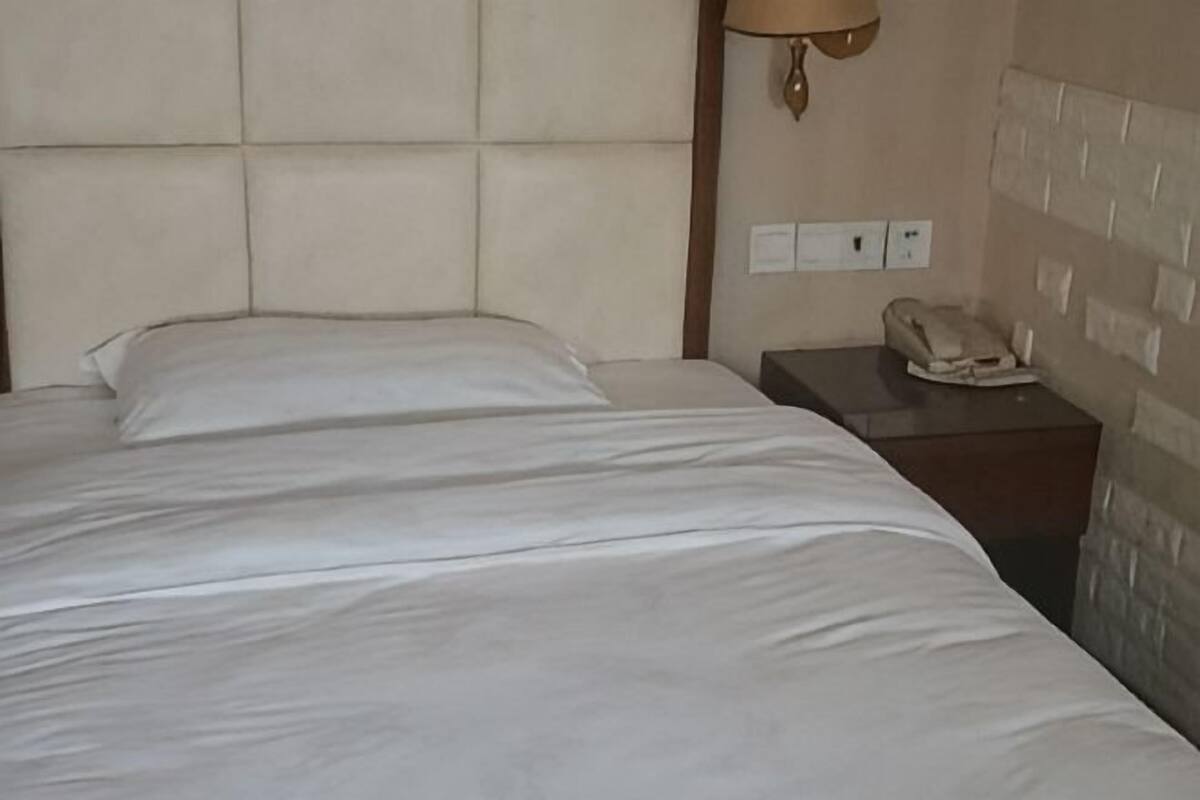 Un lit avec une tête de lit, une table de chevet avec une lampe et une prise électrique au mur.