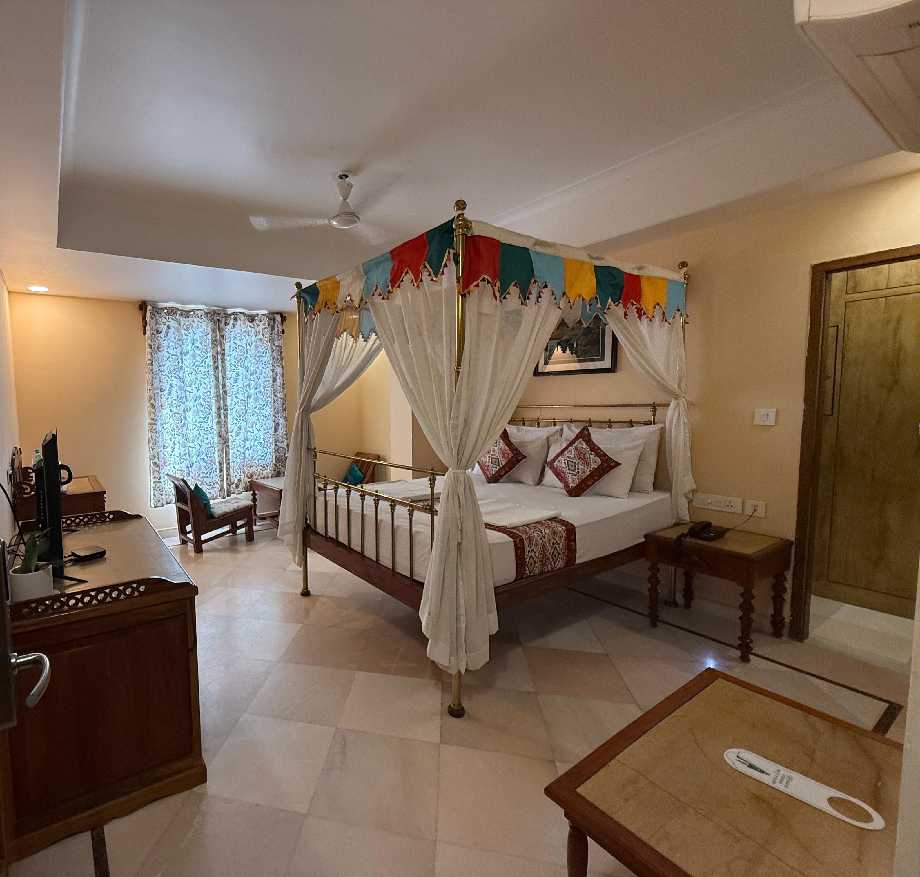 A room with a four-poster bed, a desk, a chair, and a bedside table.