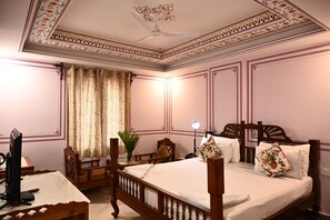 A bedroom with a wooden bed, a desk with a computer, a ceiling fan, and a window with curtains. - Hotel Rime Vista (Jaipur)