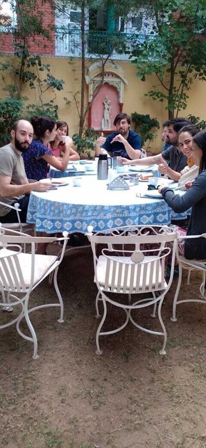 A group of people seated around a round table with a patterned tablecloth, in an outdoor setting with metal chairs and a statue in the background. - Hotel Rime Vista (Jaipur)