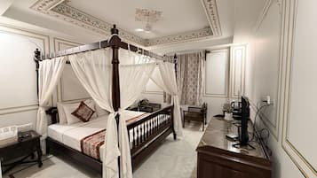 Una cama con dosel y cuatro columnas, con una mesita de noche, un aparador de madera y un escritorio con una silla.