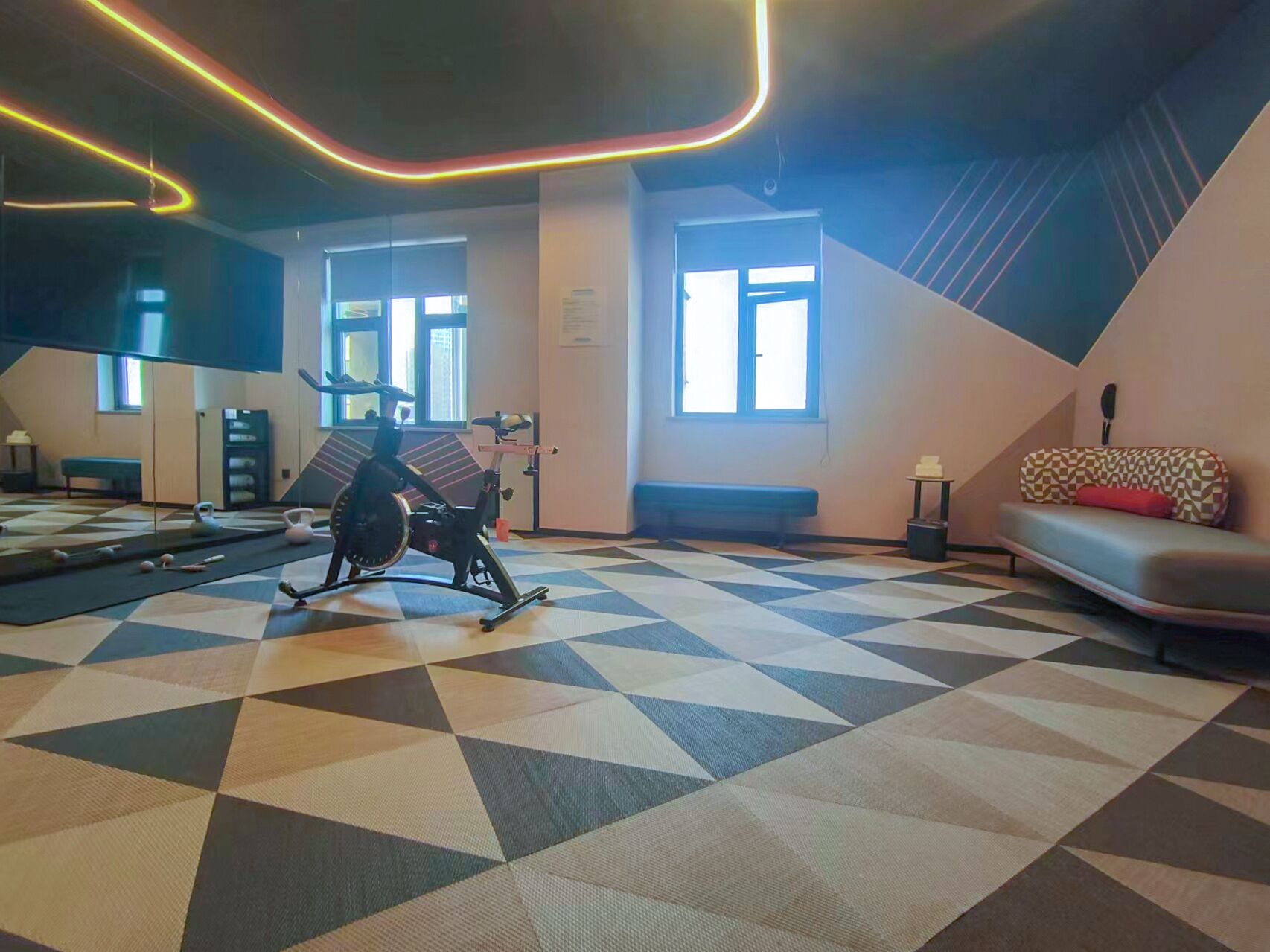 A gym with exercise equipment, a patterned floor, and a bench.