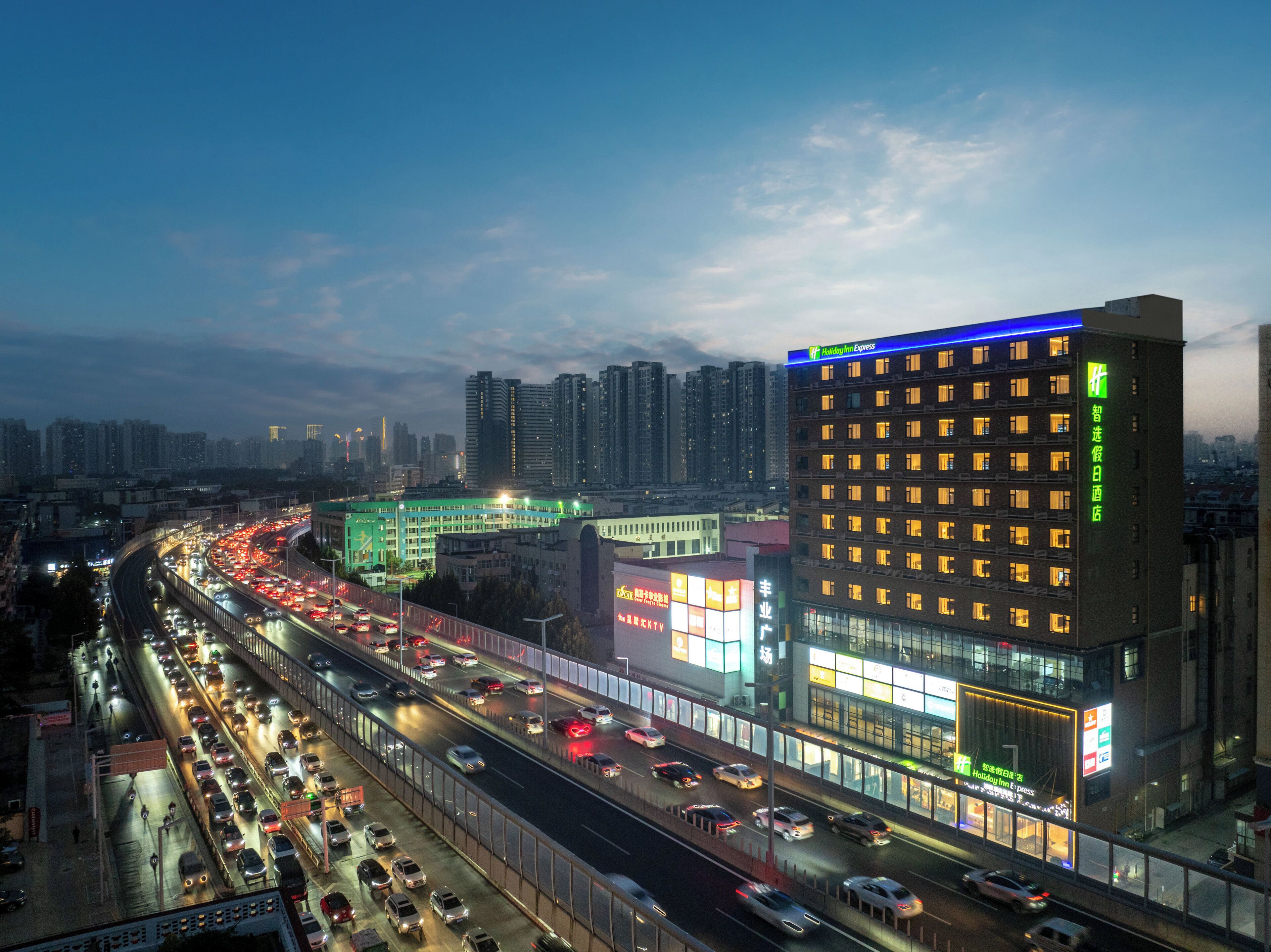 Un hotel de varios pisos con señalización iluminada, una autopista con tráfico y edificios altos al fondo.