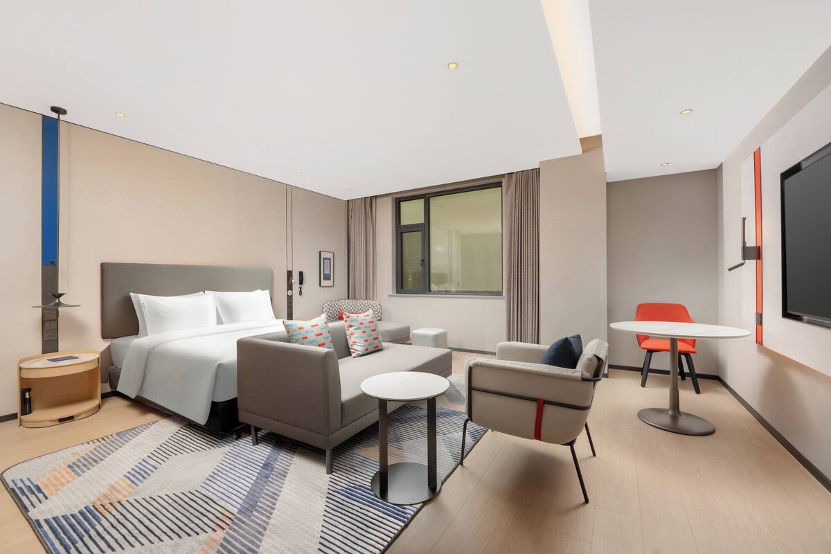 A modern hotel room with a bed, sofa, armchair, and a small table.