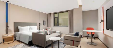 Une chambre d’hôtel moderne, équipée d’un lit, d’un canapé, d’un fauteuil et d’une petite table.